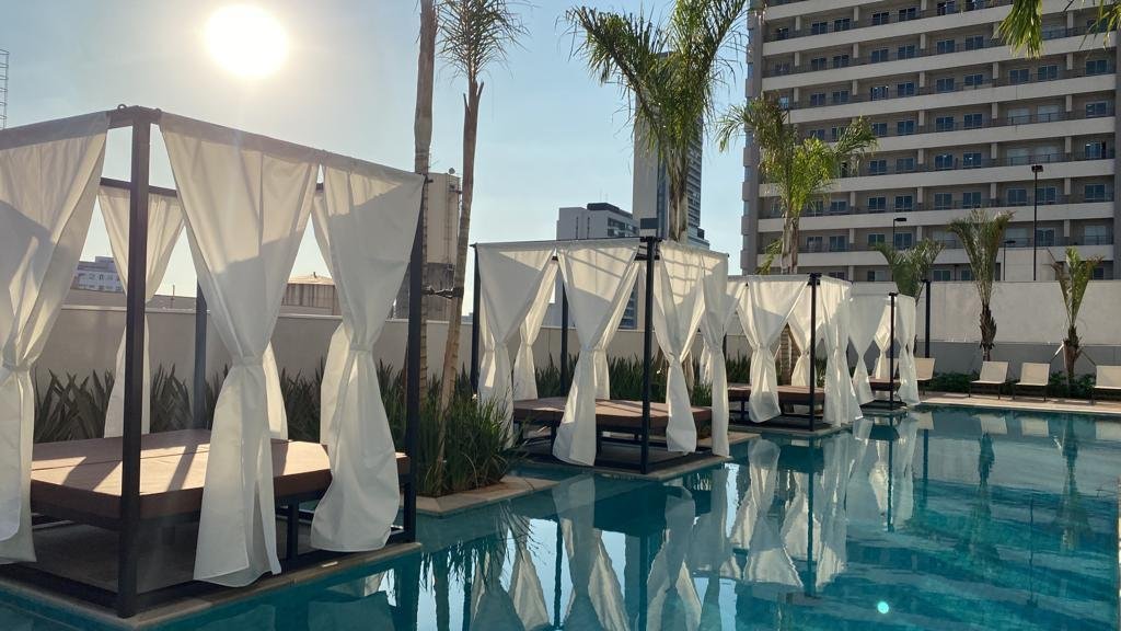 Daybeds com cortinas brancas dentro da piscina de um condomínio