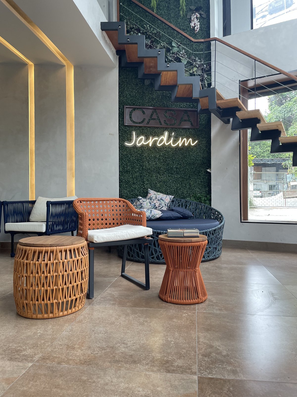 Lounge com poltrona em corda laranja, mesas laterais trançadas e sofá azul