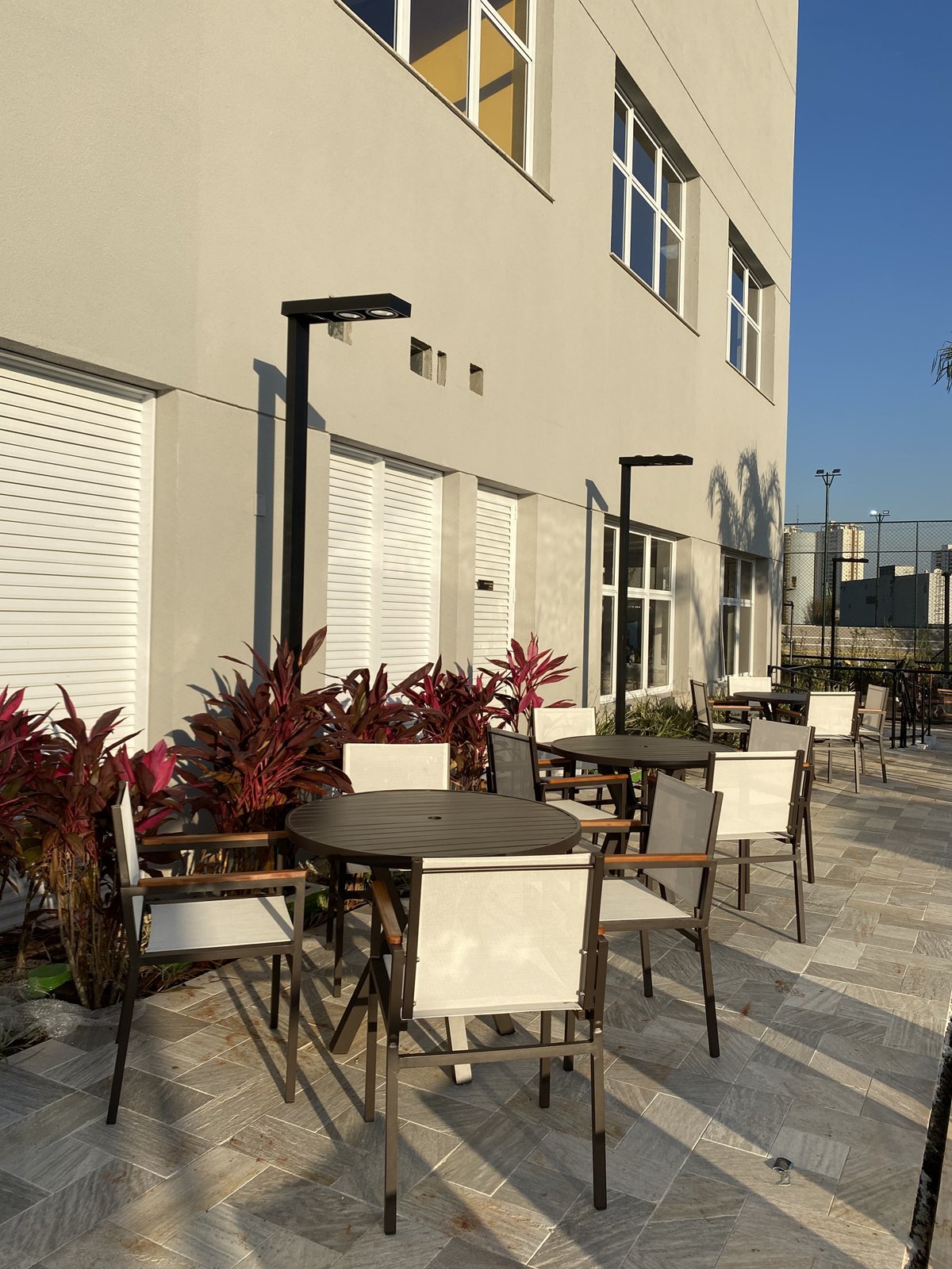 Terraço com mesas redondas escuras e cadeiras sling brancas