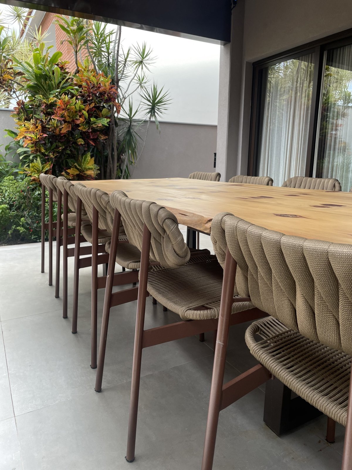 Área gourmet com mesa longa de madeira e cadeiras em corda trançada