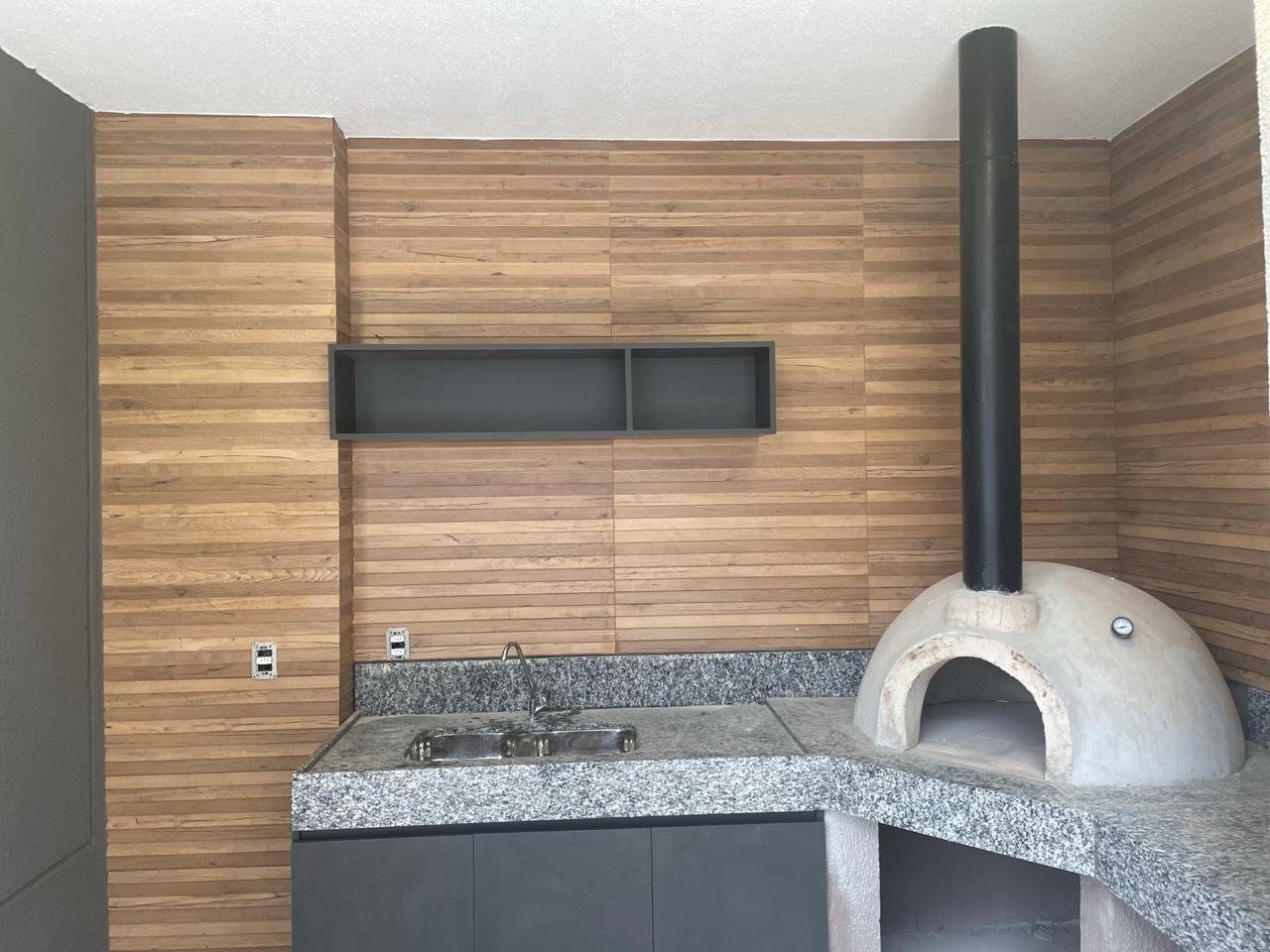 Área gourmet com painel ripado de madeira, nicho escuro e forno de pizza