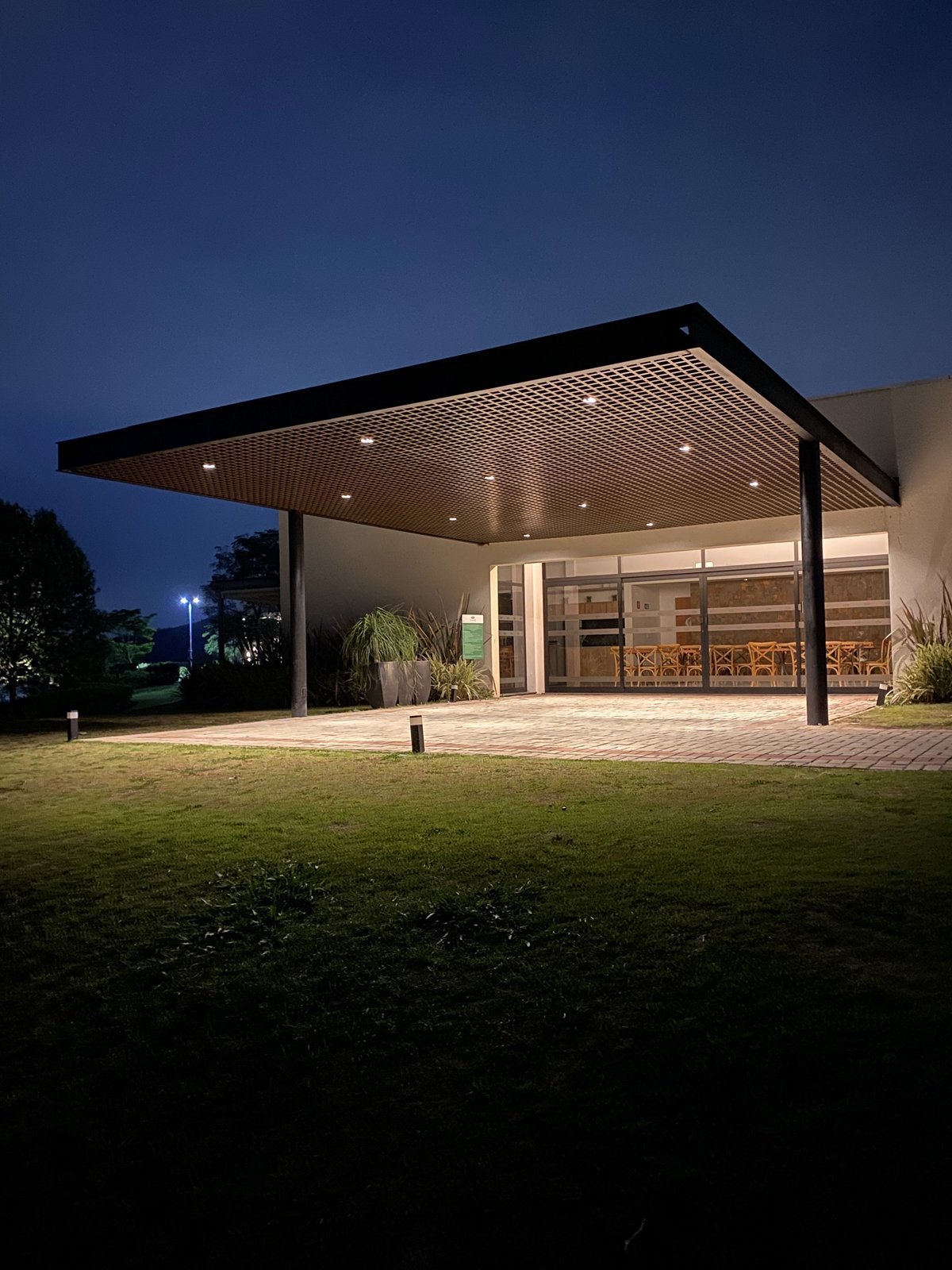 Cobertura metálica iluminada à noite sobre área externa com gramado, feita pelo Grupo NS