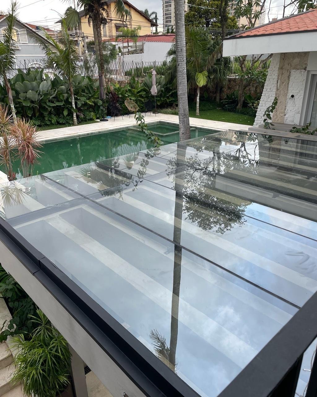 Cobertura de vidro com estrutura metálica ao lado da piscina